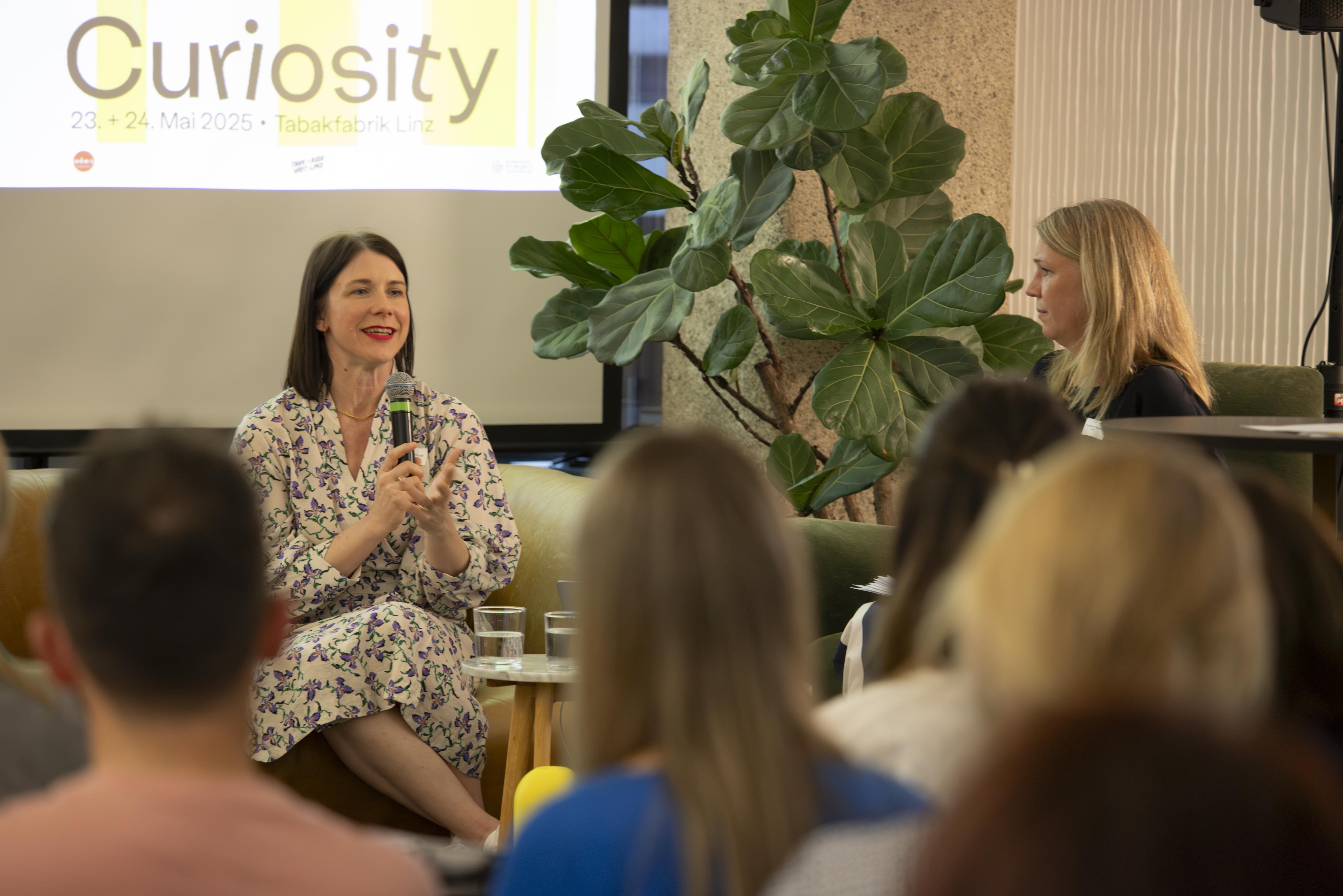 Eine Sprecherin hält einen Vortrag auf der Bühne bei der HR Coworking Night, mit "Curiosity" auf der Leinwand.