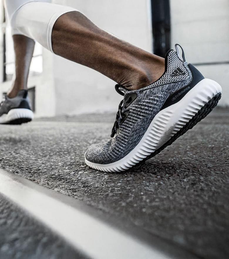 Nahaufnahme von den Beinen eines Läufers in Bewegung, die Person trägt graue Adidas Schuhe.