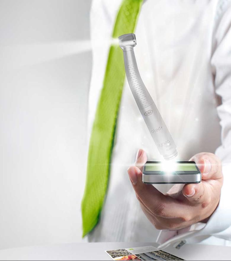 Ein Mann im weißen Laborkittel hält ein beleuchtetes W&H Dentalhandstück – Symbol für Präzision und Innovation.