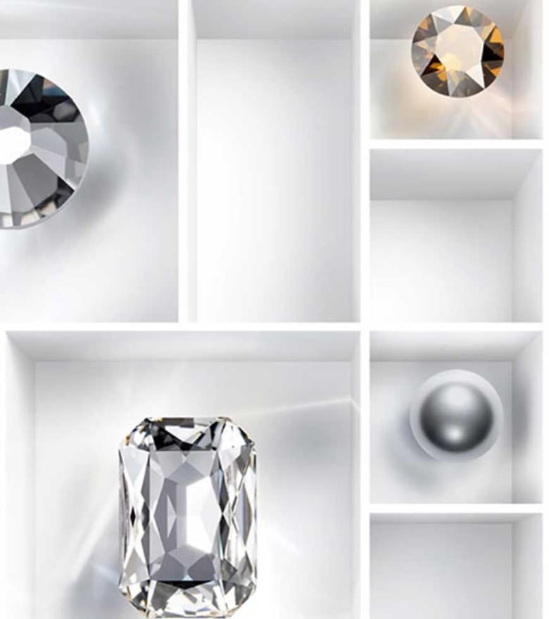 Verschiedene geschliffene Swarovski Kristalle in unterschiedlichen Formen und Farben, arrangiert in einem weißen Fächerkasten.