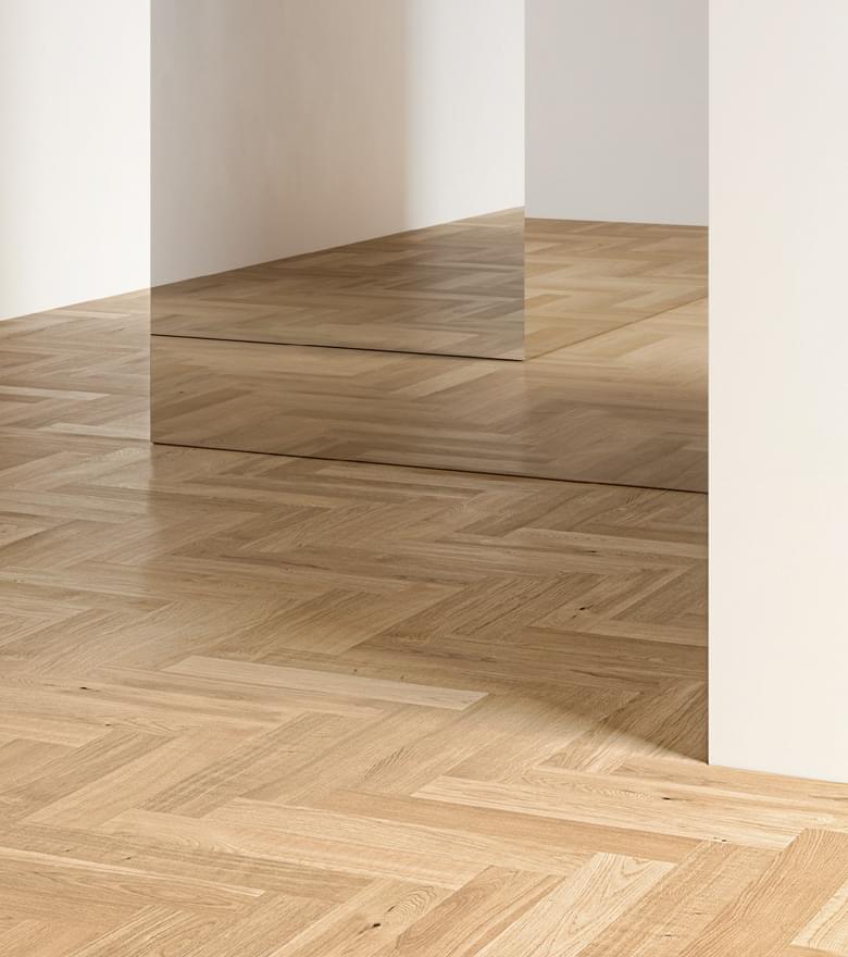 In einem minimalistisch gestalteten Innenraum reflektiert ein heller Fischgrätparkettboden die Spiegelung an einer Wand.