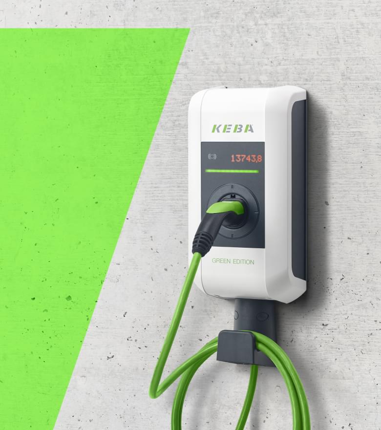 Weiße E-Ladestation mit grünem Ladekabel an einer Betonwand.