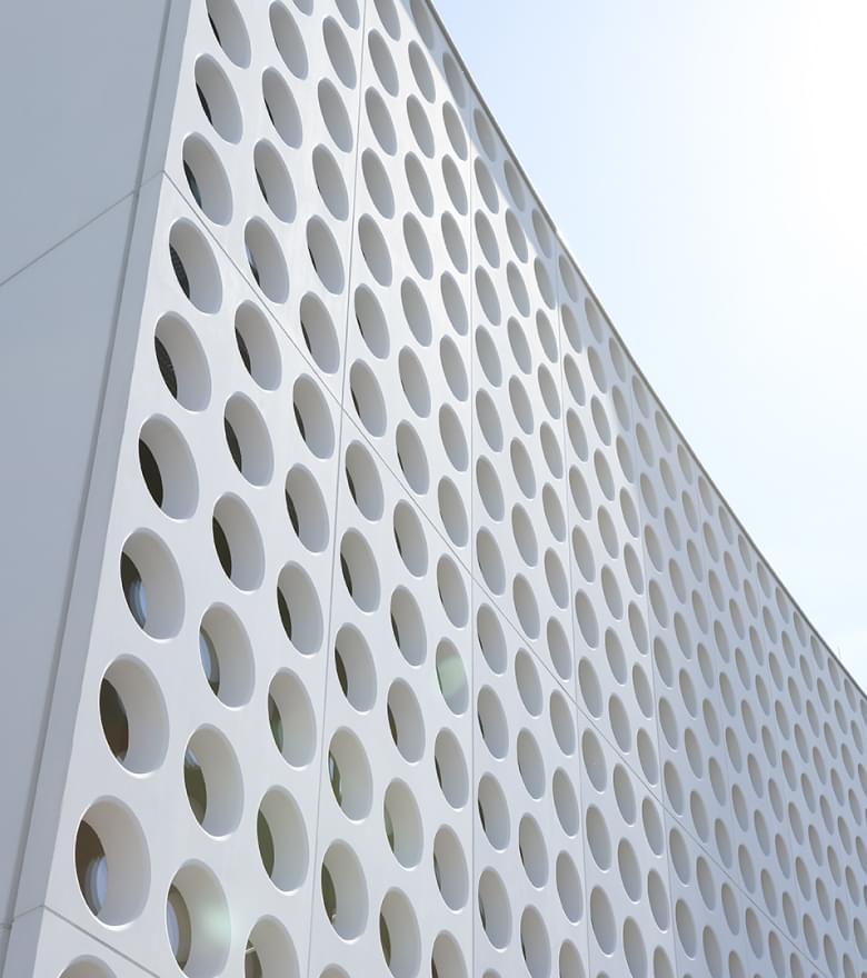 Ansicht der weißen, perforierten Fassade des Silhouette Lens Lab mit runden Öffnungen.