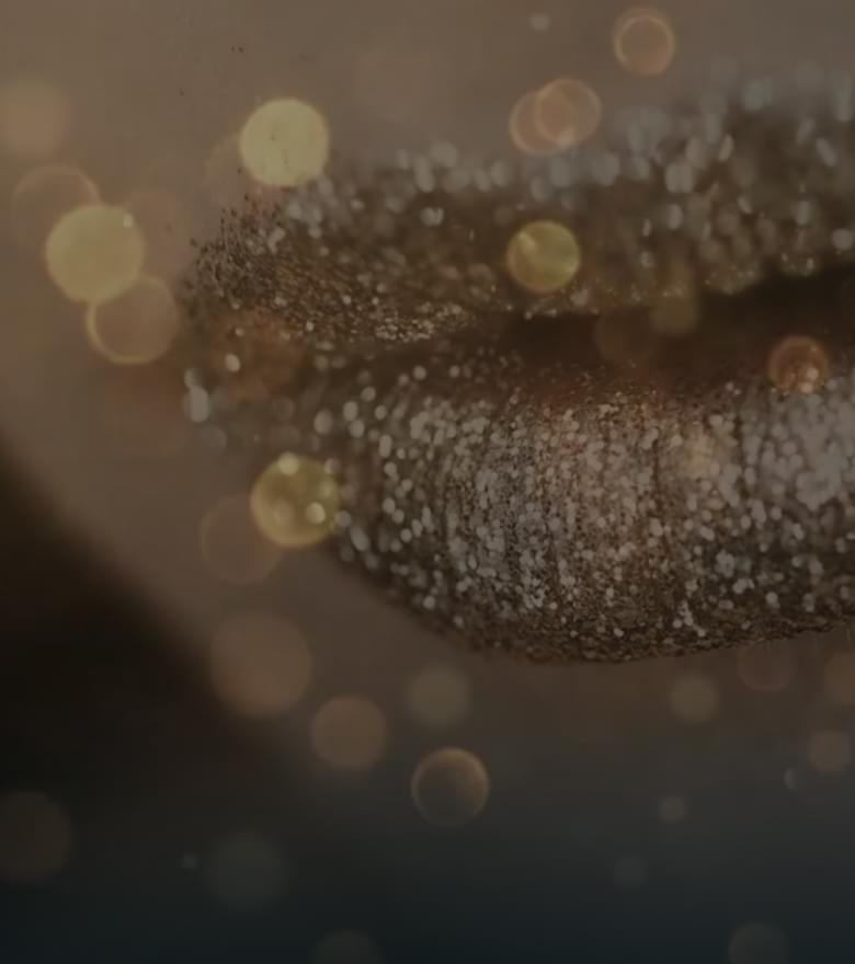 Nahaufnahme von Lippen mit goldenem Glitzer Make-up, umgeben von funkelnden Lichtpunkten.