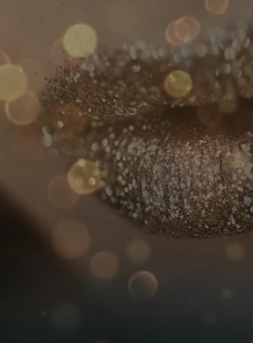 Nahaufnahme von Lippen mit goldenem Glitzer Make-up, umgeben von funkelnden Lichtpunkten.