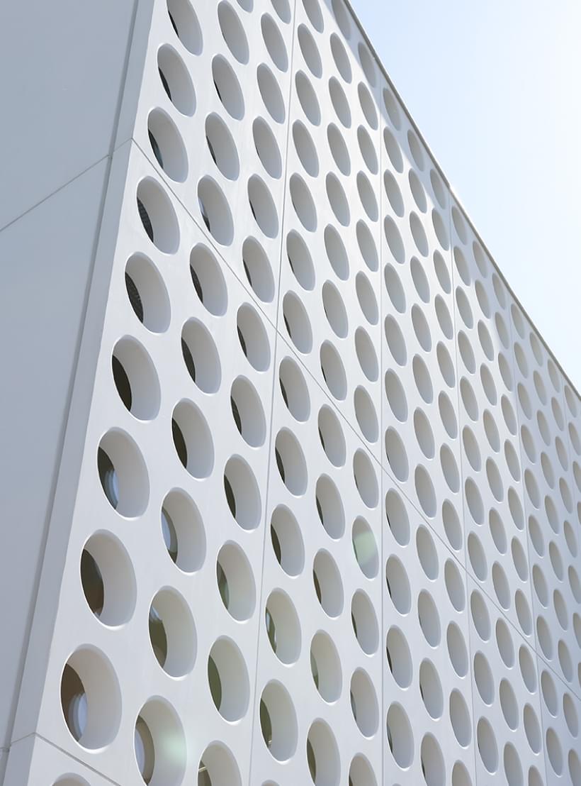 Ansicht der weißen, perforierten Fassade des Silhouette Lens Lab mit runden Öffnungen.