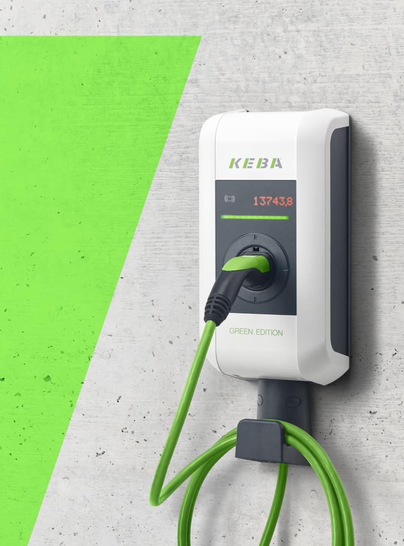 Weiße E-Ladestation mit grünem Ladekabel an einer Betonwand.