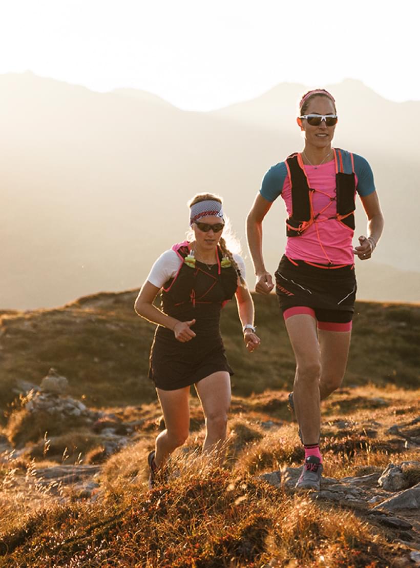 Zwei Frauen mit evil eye Sportbrillen laufen in einer Berglandschaft.