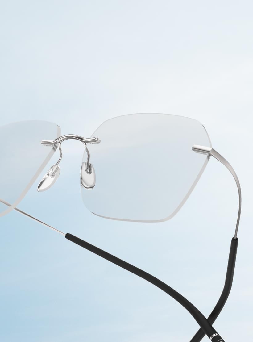 Eine moderne randlose Brille von Silhouette schwebt vor einem hellblauen Himmel.