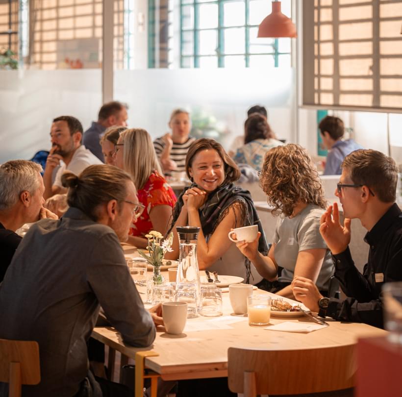 Teilnehmende des „KI Impulsfrühstücks“ von Netural sitzen gemeinsam am Tisch und unterhalten sich bei Kaffee.