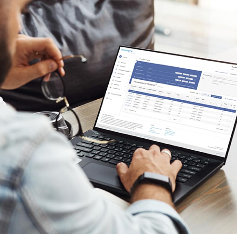 Ein Mann arbeitet an einem Laptop mit geöffnetem Dashboard und hält dabei seine Brille in der Hand.