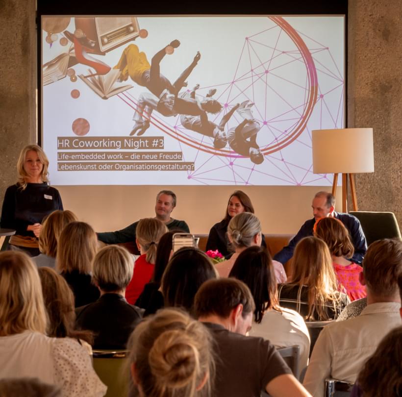 Irene Bouchal-Gahleitner spricht vor Publikum, hinter ihr die Präsentation „Life-embedded work“.