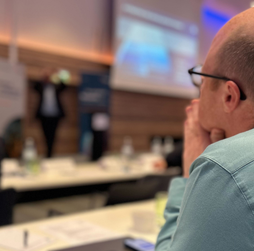 Norbert Täubl (Netural) hört im Vordergrund aufmerksam einem Vortrag auf der Bühne zu